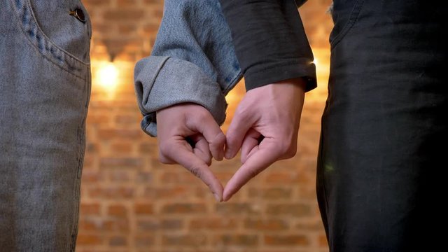 Young couble is showing heart with their arms, love sign, love conception, brick background
