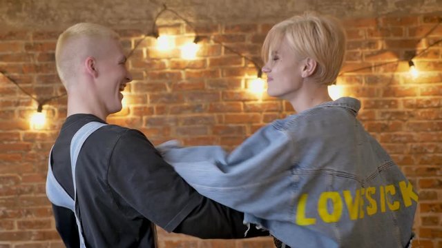 Young attractive hipster couple plays thumb wars, boyfriend wins, communication concept, brick background