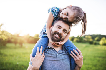 Father giving small daughter a piggyback ride in spring nature.