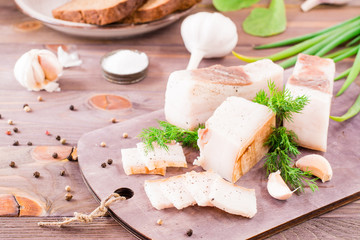 Sliced salted lard with garlic and dill on a cutting board on a wooden table