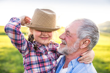 A small girl with grandfather outside in spring nature, having fun.