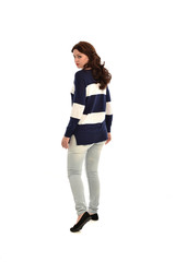 full length portrait of girl wearing striped blue and white jumper and jeans. standing pose  facing away from the camera, on white studio background