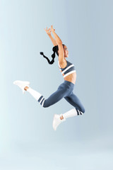 Attractive excited fitness girl dancer in sportwear jumping of joy isolated over gray background