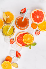 Multicolored fruit juices or smoothie in glass jars and ingredients. Top view, isolated on white background.