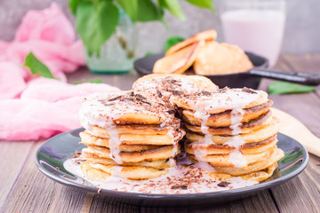 A pile of pancakes stuffed with fruit yoghurt and sprinkled with grated chocolate on a plate on a wooden table