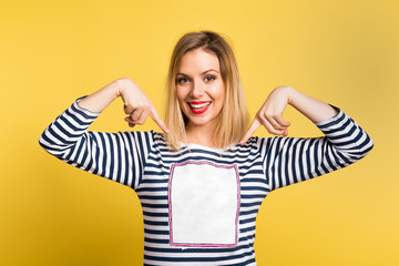 Portrait of a young beautiful woman in studio, copy space on her T-shirt. Yellow background.