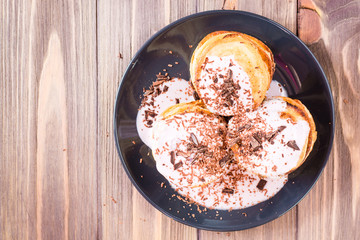 A pile of pancakes stuffed with fruit yoghurt and sprinkled with grated chocolate on a plate on a wooden table. Top view