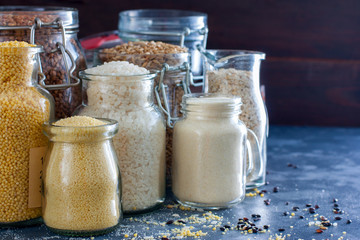 Various cereals in glass jars - rice, millet, oatmeal, couscous, buckwheat, semolina, copy space