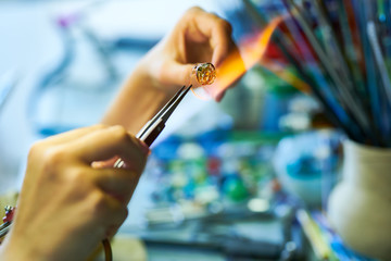 Close up of elegant female hands shaping glass over gas torch while making beads for beautiful handmade jewelry in glassworking studio, copy space