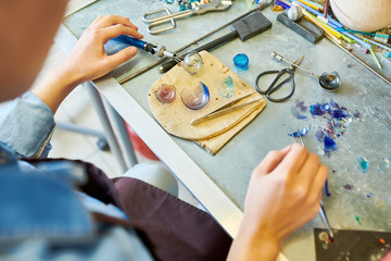 High angle crop shot of modern female artist working with glass making baubles on workstation with shattered pieces on table, copy space