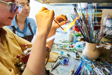 Side view crop shot of female artist  melting glass over gas torch while making handmade beads in modern creative workshop, copy space