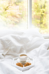 Early morning breakfast in bed, coffee and croissant on the tray
