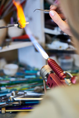 Closeup of female hands melting glass over gas torch while making handmade beads in modern creative workshop, copy space