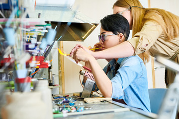 Portrait of two young women melting glass over gas torch while making handmade beads in modern creative workshop, copy space