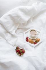Early morning breakfast in bed, coffee and croissant with strawb