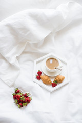 Early morning breakfast in bed, coffee and croissant with strawb