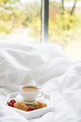 Early morning breakfast in bed, coffee and croissant with strawb