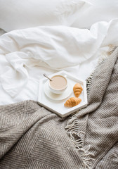 Cozy breakfast in bed, cup of coffee and croissants on white and