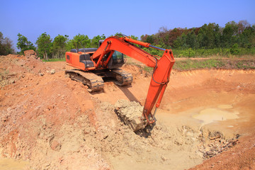 red machinery digging red soil is  big hole on blue sky and green tree background outdoor