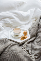 Cozy breakfast in bed, cup of coffee and croissants on white and