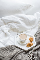 Cozy breakfast in bed, cup of coffee and croissants on white and