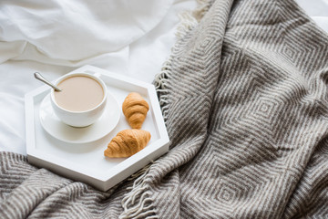 Cozy breakfast in bed, cup of coffee and croissants on white and