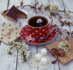 Sugar, cake, diary, red spotted cup of tea and blooming tree branches on planks. Spring still life, beautiful rural background with seasonal flowers in vintage style