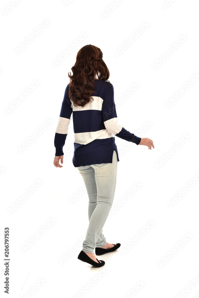 Wall mural full length portrait of girl wearing striped blue and white jumper and jeans. standing pose  facing away from the camera, on white studio background