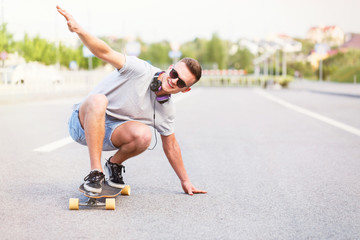 Skateboarder in sunglasses rides longboard on asphalt road in the city, low position trick ride