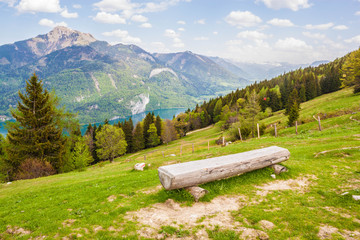 Log bench on a slope of a mountain Zwoelferhorn in austrian alps. Beautiful view of Wolfgangsee lake and Schafberg mountain on a sunny spring day.