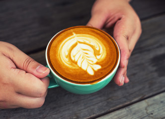 Hand women with cappuccino coffee in a green cup on wooden