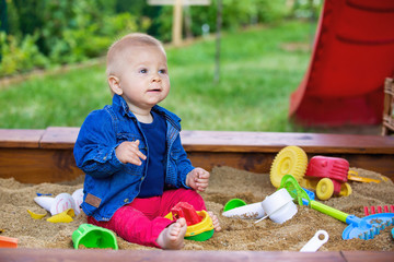 Little baby boy, playing in a sandpit with different toys