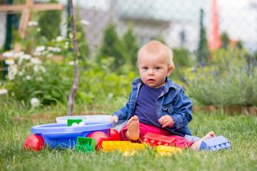 Little baby boy, playing with big construction blocks in garden