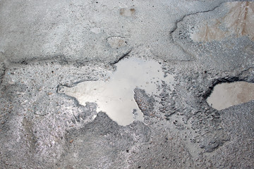 Dangerous destroyed roadbed. The bad asphalted road with a big pothole filled with water.
