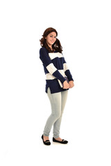 Fototapeta premium full length portrait of girl wearing striped blue and white jumper and jeans and holding a book. standing pose on white studio background