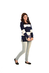 full length portrait of girl wearing striped blue and white jumper and jeans and holding a book. standing pose on white studio background