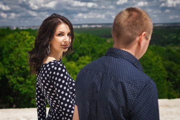 Obraz premium young teenagers walking in nature. girl with long brunette hair wearing black dress in white peas looking back, boy in blue shirt in pattern