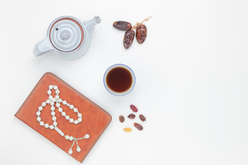 Table top view aerial image of decoration Ramadan Kareem holiday background.Flat lay dates with white rosary & cup tea.The holy book of Koran on modern white wood at office desk.Free space design.