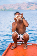 A man sitting at the boat and  blowing on a conch shell at Coron island Philippines
