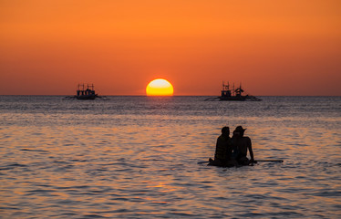 Silhouette of a pair floating on on the sup surfboard at amazing orange sunset over the sea at Boracay island Philippines