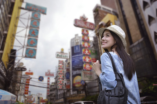 Young asian woman traveler with a backpack on her shoulder and travel hat walking on footpath over China town, Bangkok, Thailand, Travel holiday relaxation concept