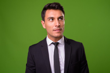 Young handsome Hispanic businessman against green background