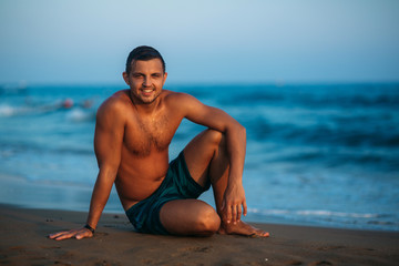 Fototapeta na wymiar Handsome man on a sandy beach sits on the seashore