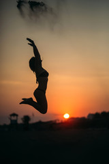 Sexy girl jumps up and throws sand. Silhouette of lady