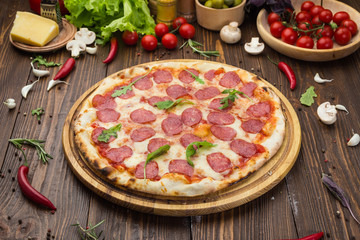 Pizza pepperoni with mozzarella cheese, salami and arugula on wooden background
