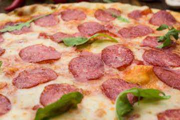 Pizza pepperoni with mozzarella cheese, salami and arugula on wooden background