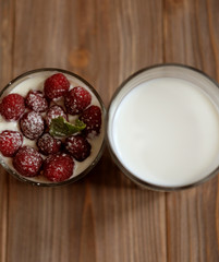 A glass of milk and granola with raspberries over wooden background, top view, close up.