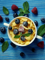 Cornflakes with berries raspberries and blueberries on blue wooden background. Top view. Close up.
