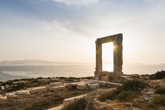 View over ruins of ancient marble doorway monument Portara at sunset in Naxos, Greece.