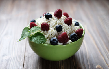 Cottage cheese in green bowl with raspberries and blueberries on wooden background. Healthy Breakfast.
